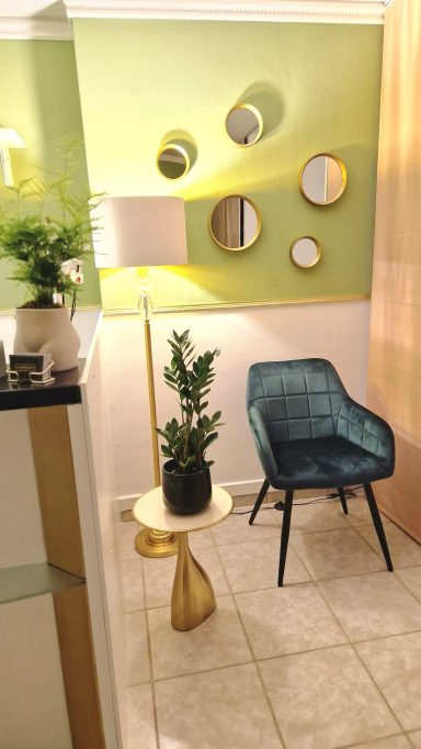 Wartebereich -2- Ein gemütlicher Raum mit grünen Wänden, Pflanzen, einem Stuhl und Spiegeln.
